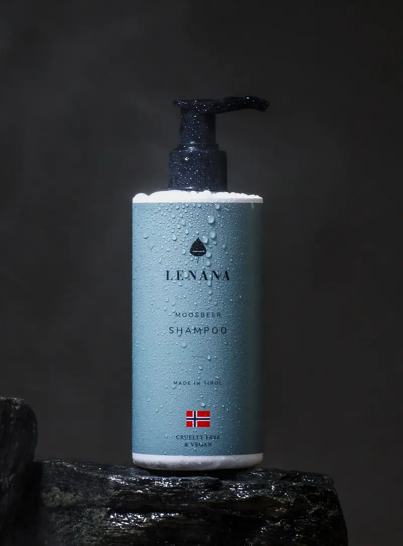 Shampoo-Flasche ist blau Farbe mit schwarzer Pumpe mit norwegischen Flagge und cruelty free &amp; vegan Label. Die Flasche ist in Wassertropfen und steht auf einem dunklen Stein