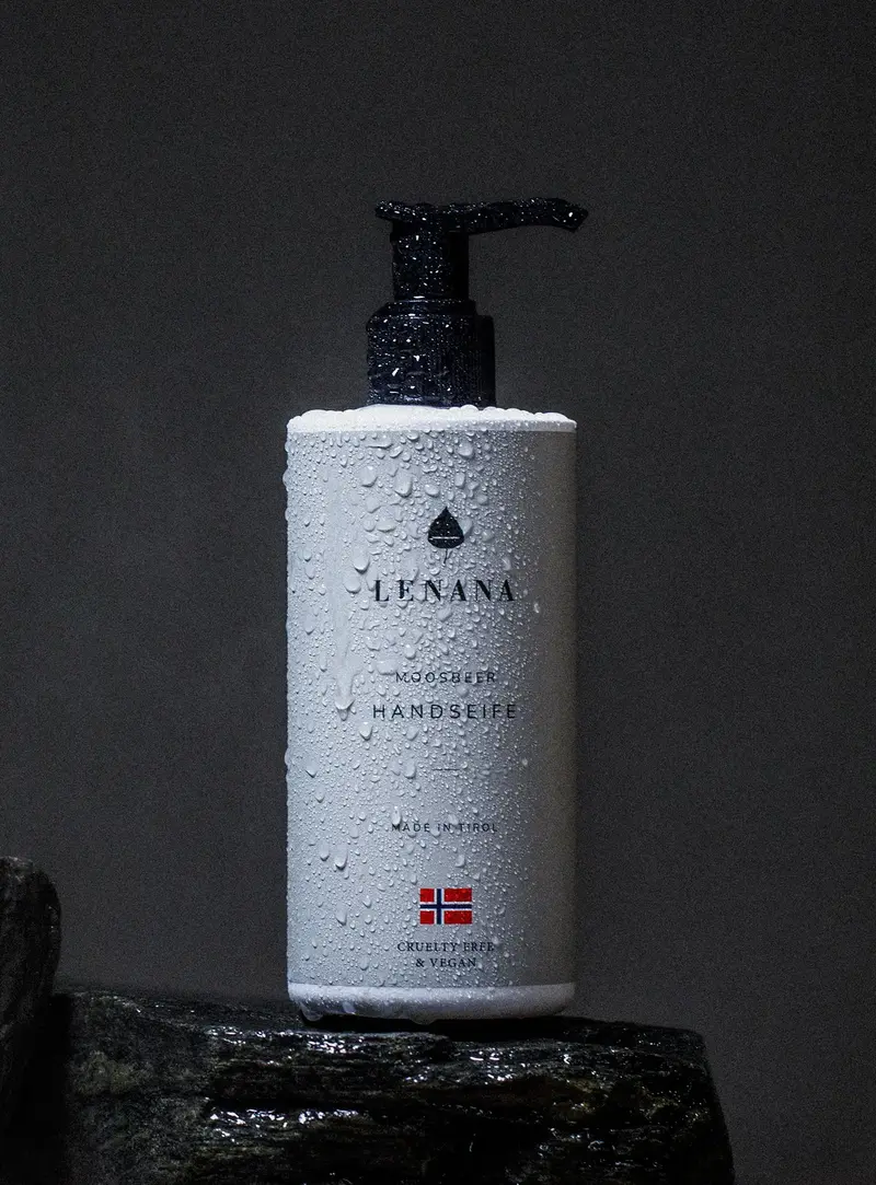 Handseife Flasche ist pastell cremefarben mit schwarzer Pumpe mit norwegischen Flagge. Die Flasche ist in Wassertropfen und steht auf einem dunklen Stein